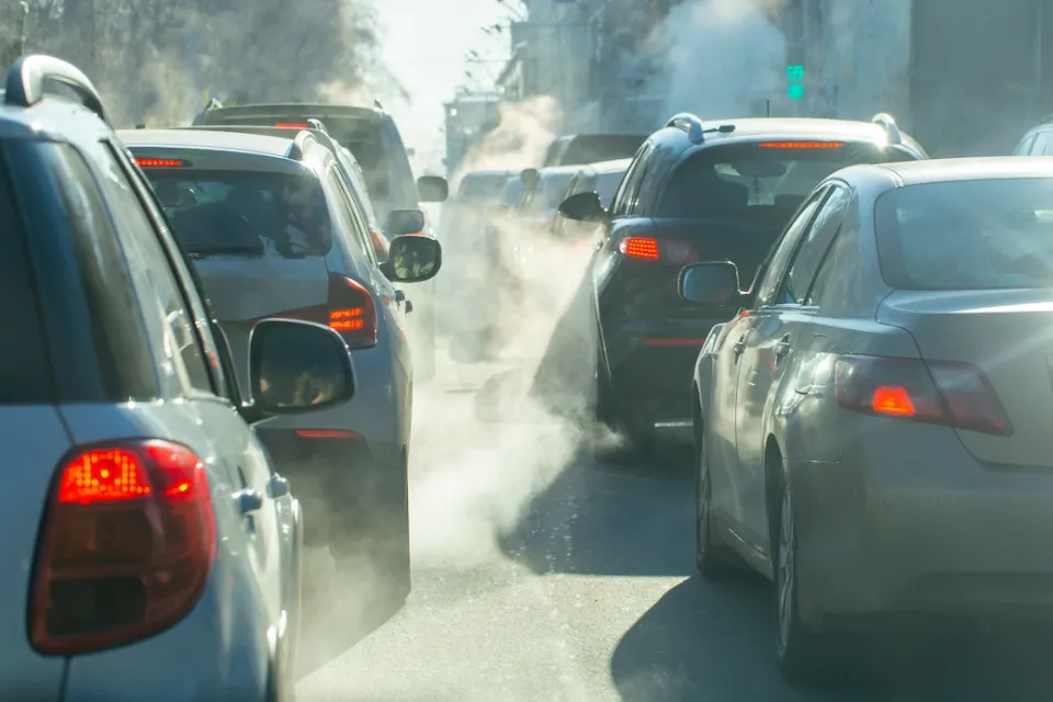Cars in busy traffic with emissions visible from exhaust pipes.